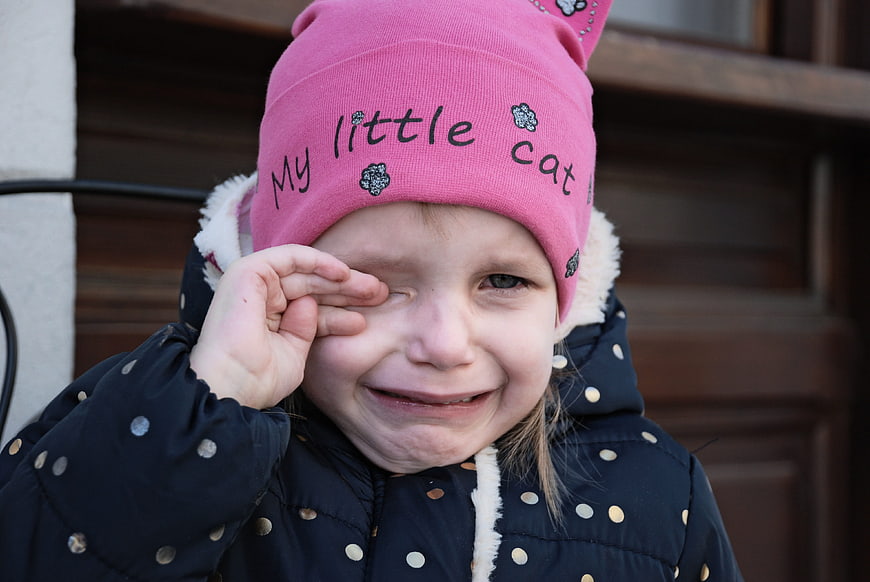 Crying little girl in pink hat wiping tears