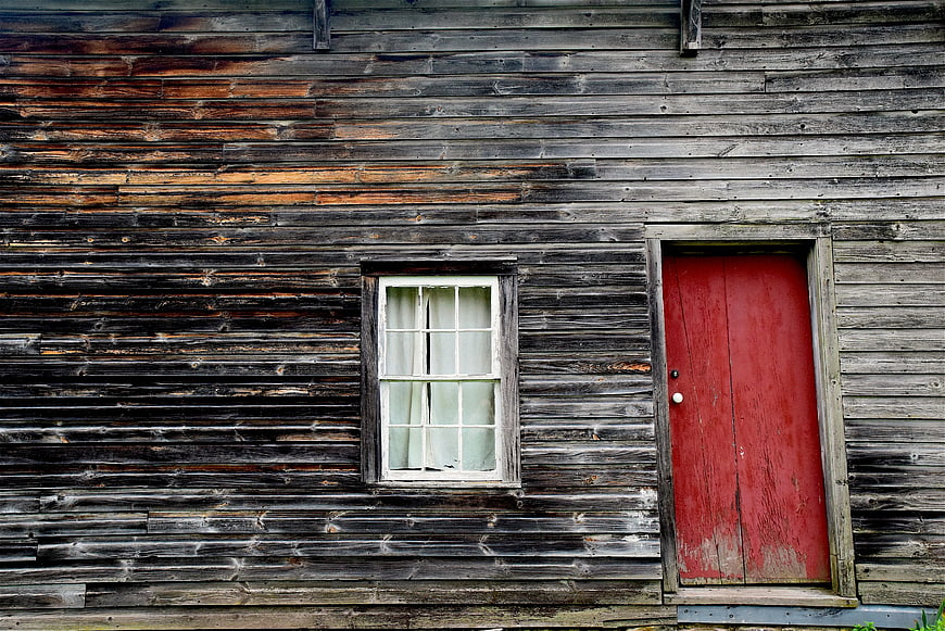 Weathered wooden wall with red door and white window