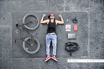 Top view of young man lying on asphalt with bicycle and laptop