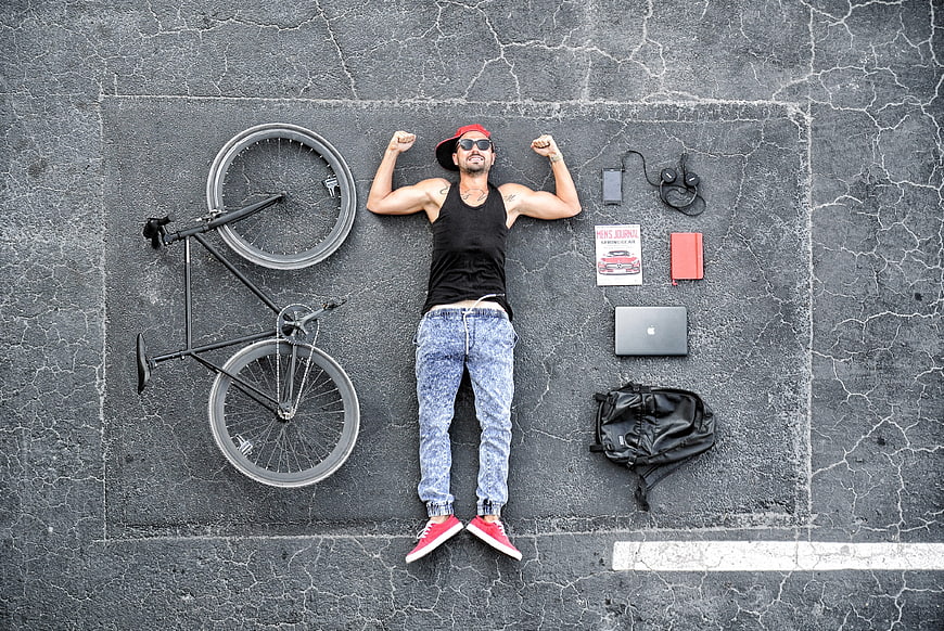 Top view of young man lying on asphalt with bicycle and laptop