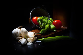 Dark moody still life of fresh garlic, tomatoes, and green peppers