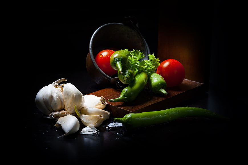 Dark moody still life of fresh garlic, tomatoes, and green peppers