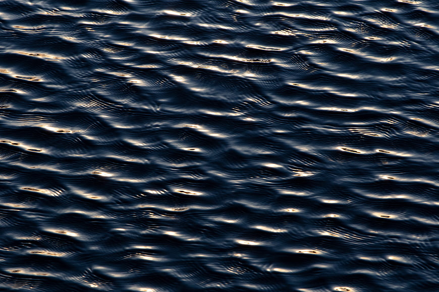 Dark Blue Water Ripples with Golden Sunlight Reflections