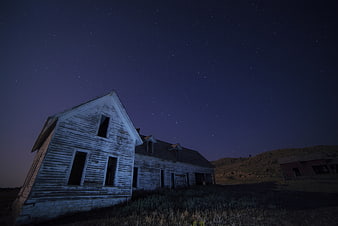 Abandoned white farmhouse under starry night sky