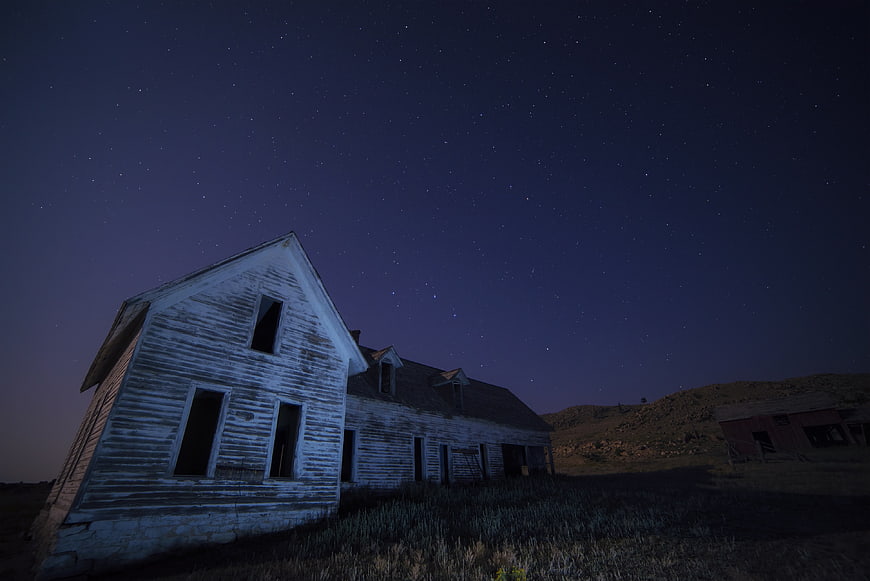 Abandoned white farmhouse under starry night sky