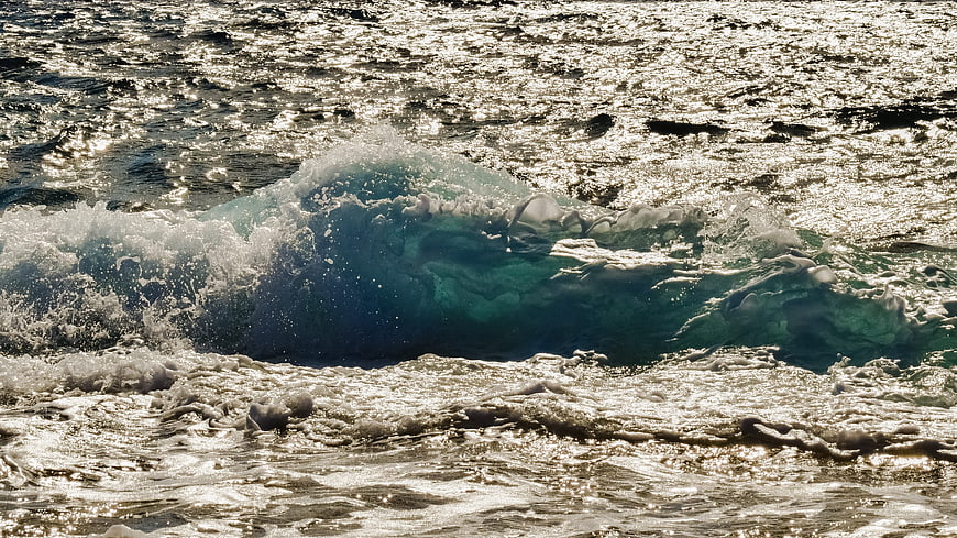 Ocean wave crashing with sparkling sunlight on water surface