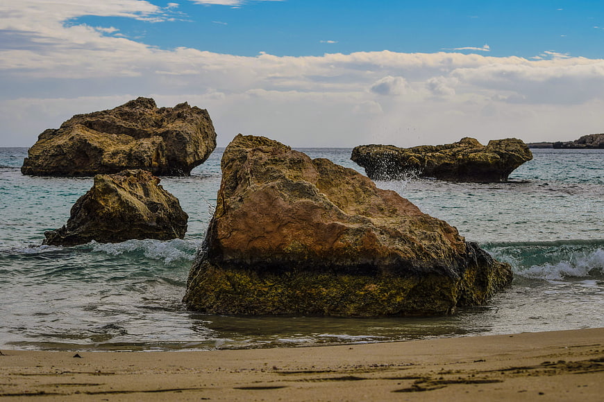 Rugged coastal rocks in turquoise sea with sandy beach