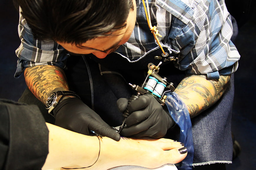 Tattoo artist inking a foot design with a machine
