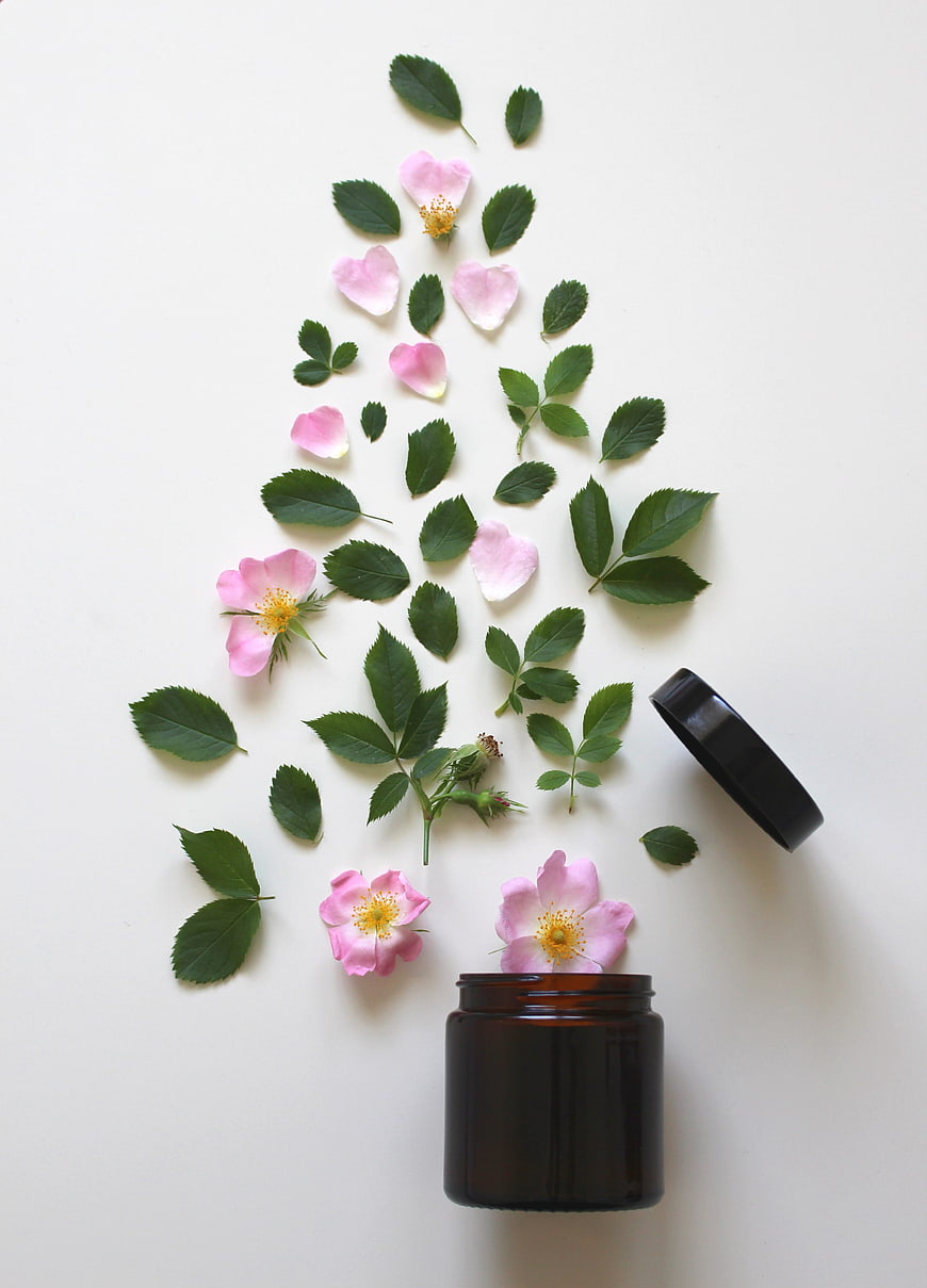 Pink Rose Blossoms and Leaves Arranged Above Amber Cosmetic Jar