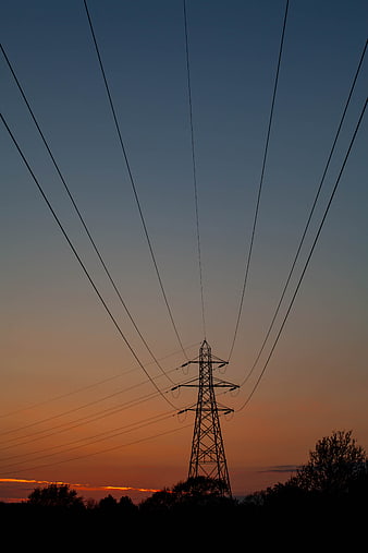 Silhouette of electricity pylon against orange sunset sky