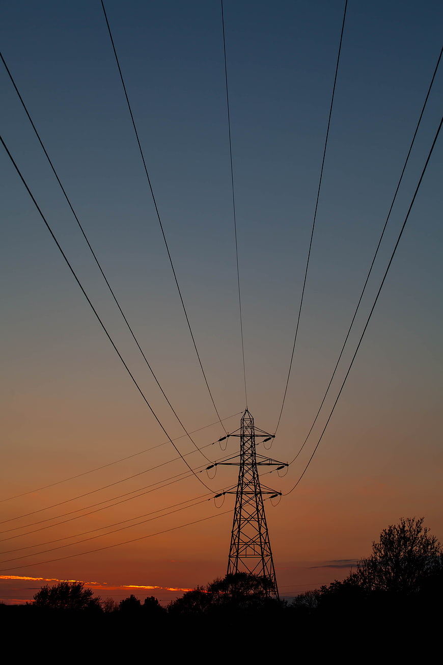Silhouette of electricity pylon against orange sunset sky