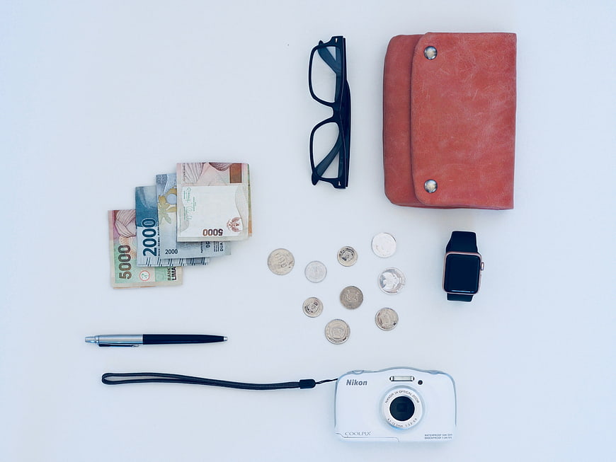 Flat lay of daily essentials including camera, wallet, and cash