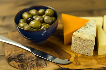 Artisan Cheese Wedges and Green Olives on Rustic Wooden Board