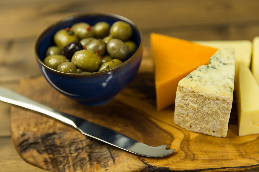 Artisan Cheese Wedges and Green Olives on Rustic Wooden Board