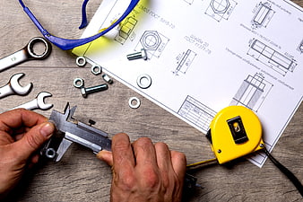 Hands measuring nut with calipers on blueprint