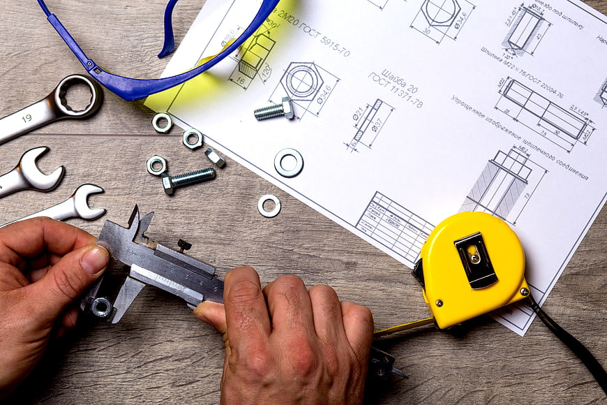 Hands measuring nut with calipers on blueprint
