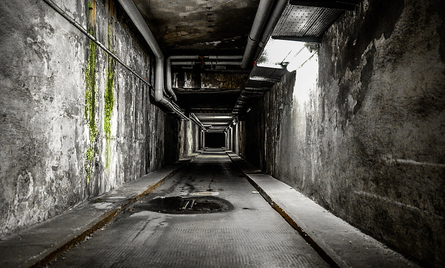 Dark atmospheric concrete tunnel with pipes and moss