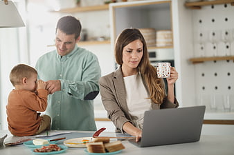 Mother working on laptop while father plays with toddler at breakfast