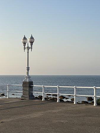 Vintage white lamp post on seaside promenade with ocean view