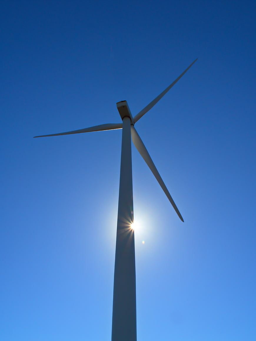 Wind Turbine Silhouette Against Blue Sky with Sun Flare
