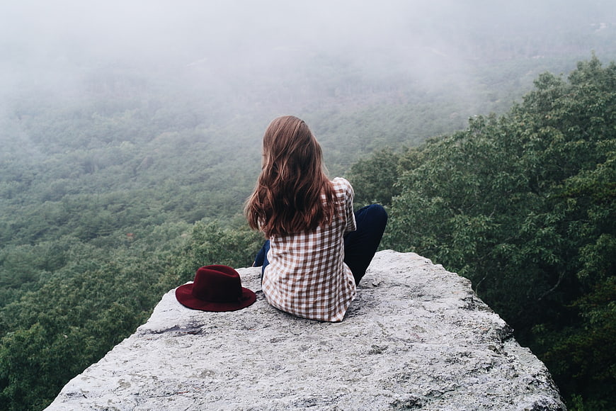 Woman sitting on cliff edge overlooking misty forest landscape