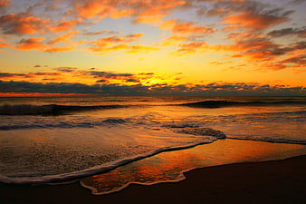 Vibrant Orange Sunrise Over Ocean Waves On Sandy Beach