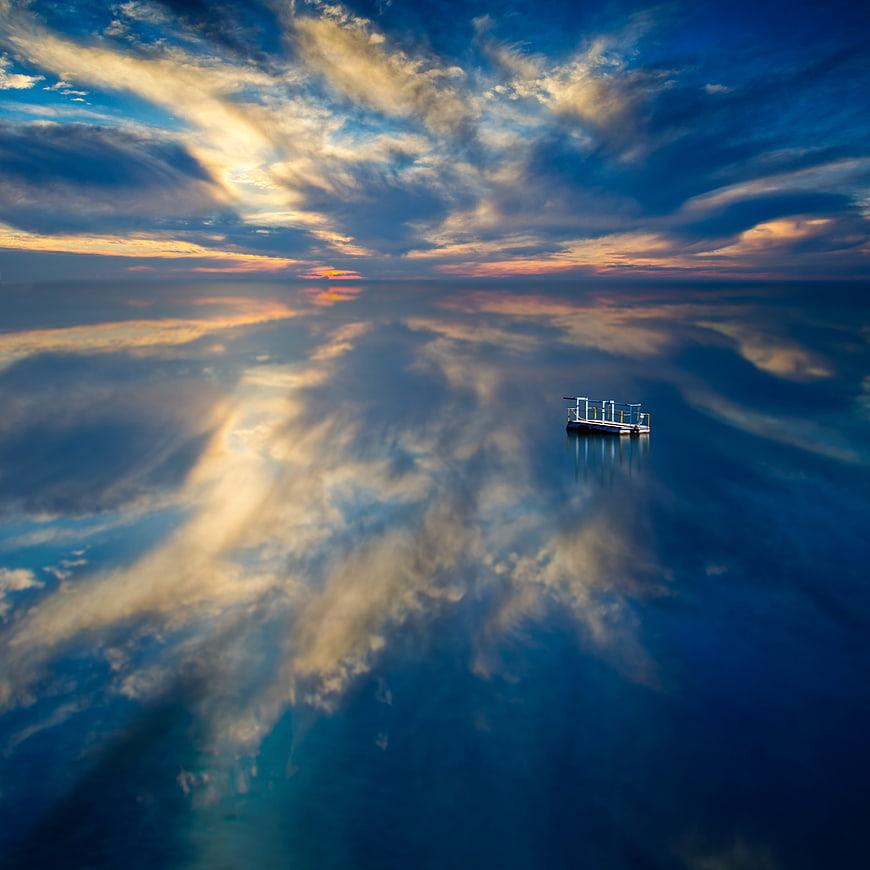 Serene Sunset Seascape with Boat Reflection on Calm Water