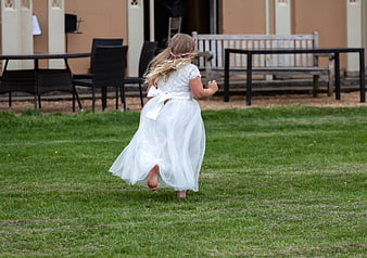Little girl in white dress running barefoot on grass