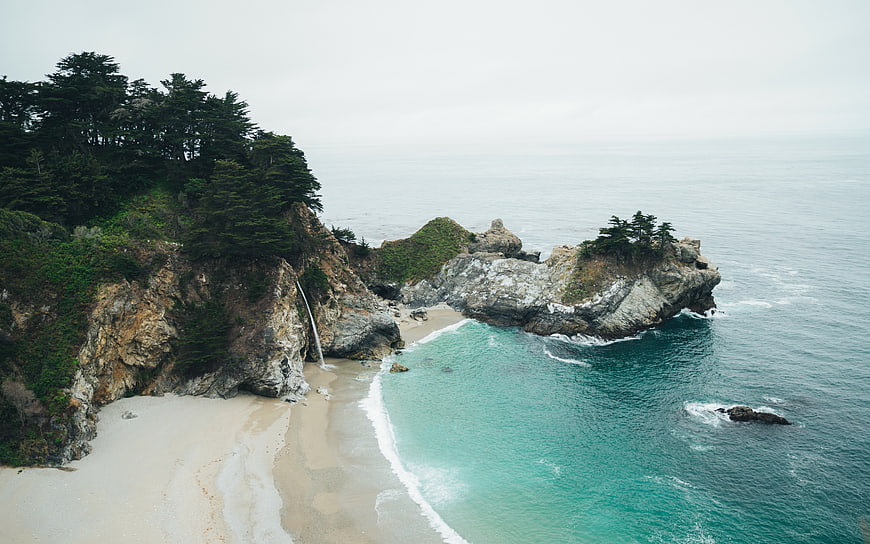 Aerial View of Secluded Coastal Beach with Waterfall and Cliffs
