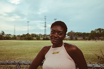 Portrait of young black woman leaning on fence at sports field