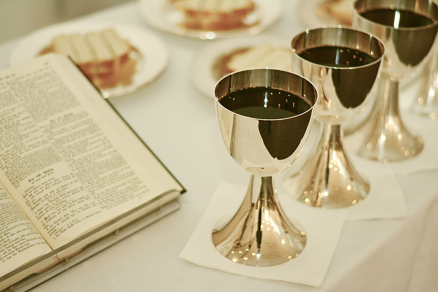 Silver chalices with wine and open Bible on white table