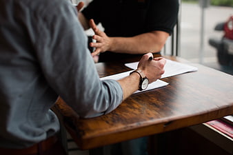 Two Men Discussing Documents At Wooden Table