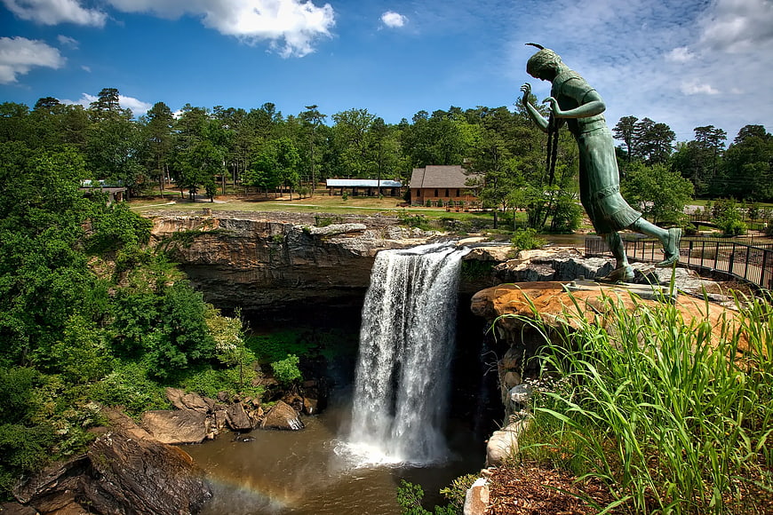 Statue overlooking waterfall in lush green park