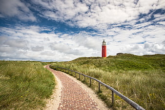 Red Lighthouse on Green Dunes with Brick Pathway