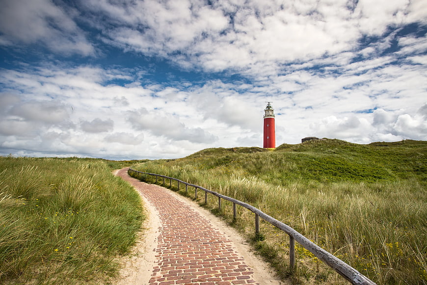 Red Lighthouse on Green Dunes with Brick Pathway