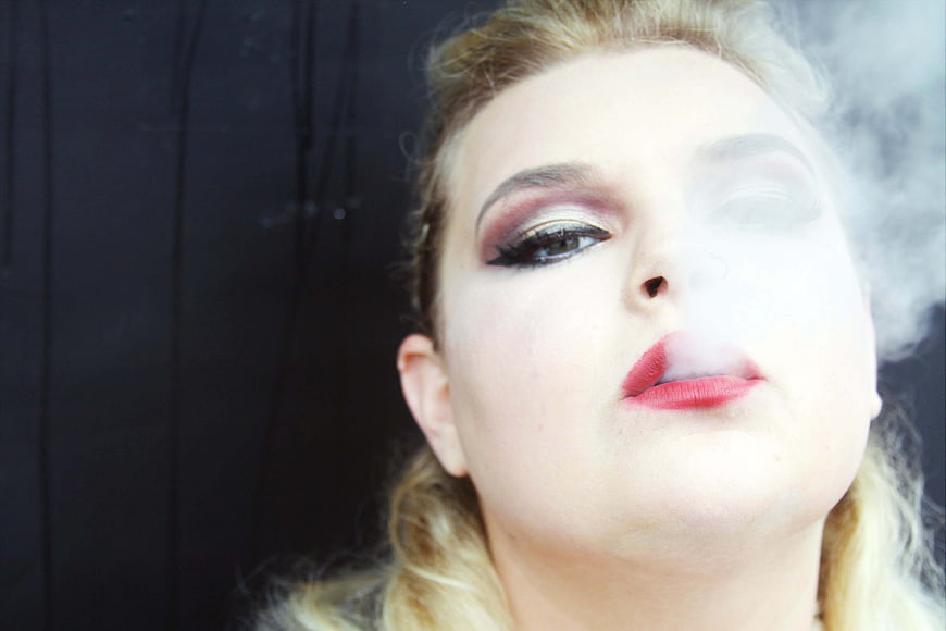 Close-up portrait of woman exhaling smoke with dramatic makeup