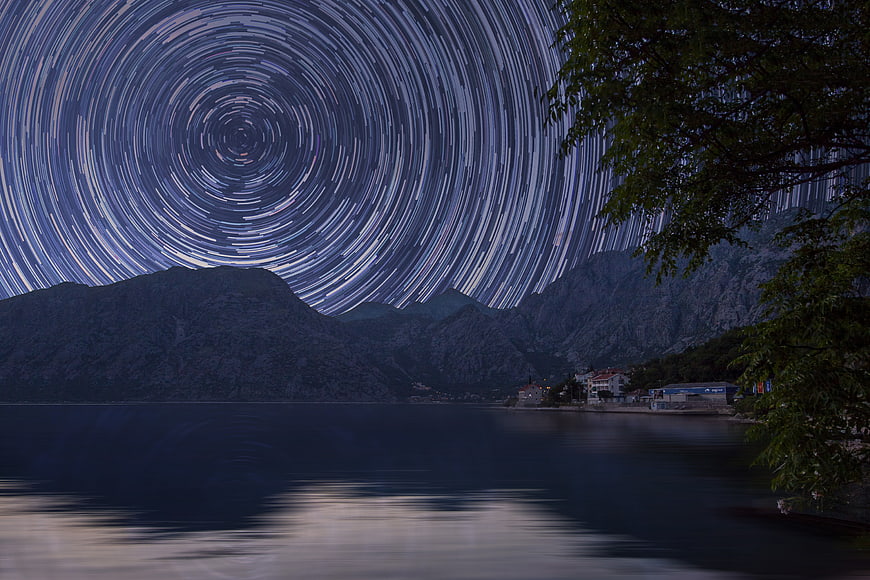 Star trails over a coastal mountain landscape at night