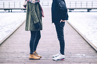Couple standing on wooden pier in winter coats and boots
