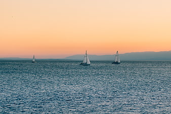 Sailboats on Calm Sea at Sunset with Distant Mountains