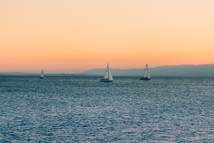 Sailboats on Calm Sea at Sunset with Distant Mountains