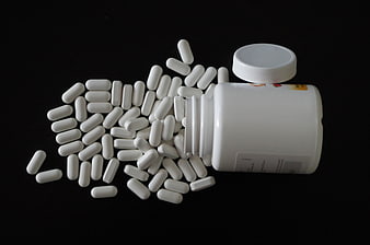White Capsules Spilling From Plastic Bottle On Black Background