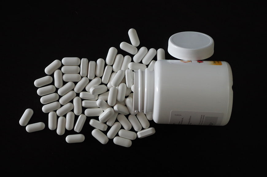 White Capsules Spilling From Plastic Bottle On Black Background