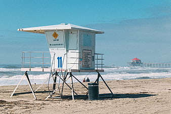 White Lifeguard Tower on Sandy Beach with Pier in Background