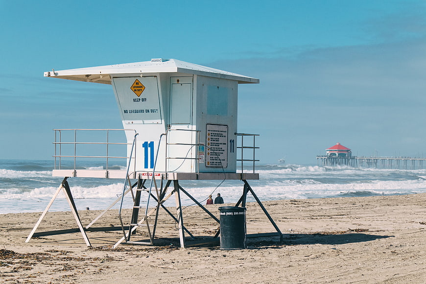 White Lifeguard Tower on Sandy Beach with Pier in Background