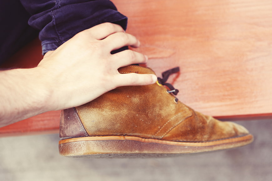 Close-up of hand resting on brown suede shoe on wooden bench