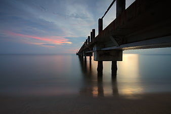 Long Exposure Sunset Under Wooden Pier on Calm Ocean