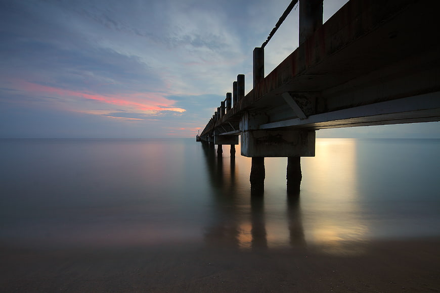 Long Exposure Sunset Under Wooden Pier on Calm Ocean
