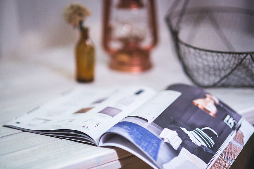Open fashion magazine on white wooden table with decor
