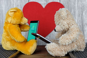 Two teddy bears holding smartphones with WhatsApp app and red heart background