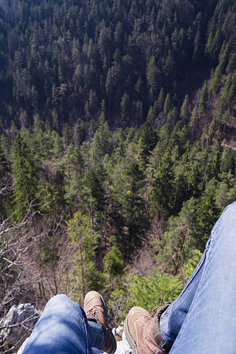 Hiker's legs dangling over a forested mountain cliff